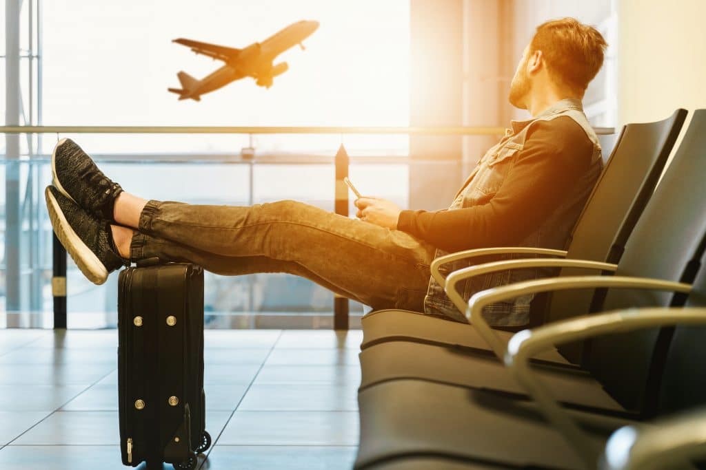Man waits in airport as plane takes off in the background