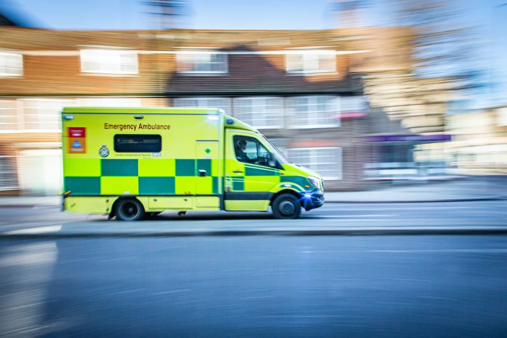 Ambulance driving along a road in front of houses